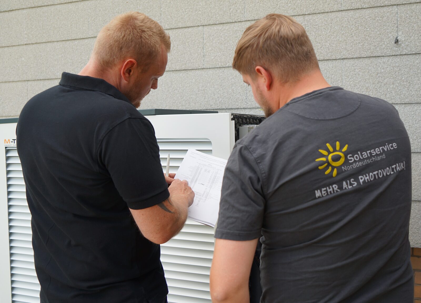 Zwei Monteure von Solarservice Norddeutschland prüfen den Anschlussplan an einer M-TEC Wärmepumpe